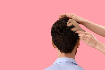 Fototapeta premium Female hairdresser combing hair of young man on pink background, back view