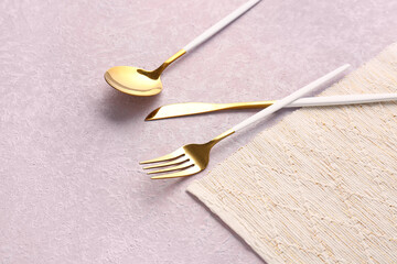 Golden cutlery with white handles on lilac background