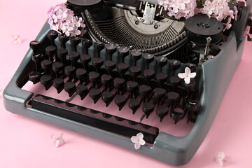 Vintage typewriter with lilac flowers on pink background, closeup