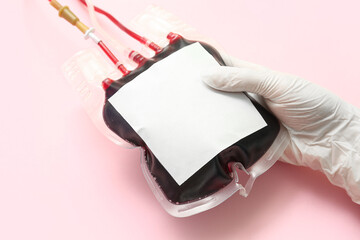 Female doctor with blood pack on pink background, closeup. World Donor Day