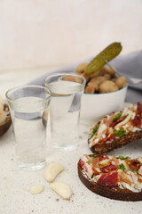 Shots with cold vodka and snacks on light background