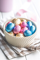Chocolate easter eggs wrapped in multi colored foil in bowl on white table.