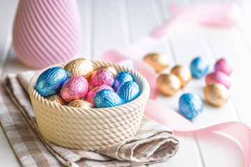 Chocolate easter eggs wrapped in multi colored foil in bowl on white table.