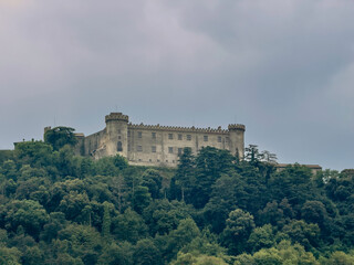 Obraz premium Lake Bracciano, Lazio, Italy - July 7, 2024: Fortress, Castello Orsini-Odescalchi, on hill above the lake. Forest on the hill under cloudscape