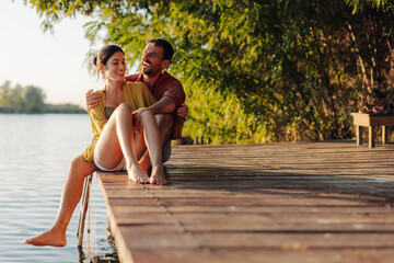 Happy couple relaxing on lake pier at sunset, enjoying summer vacation