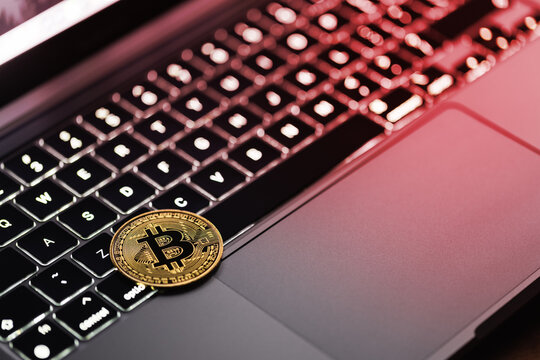 Bitcoin coin lying on the computer keyboard, around a red color indicating price declines