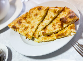 Georgian national delicious flatbread khachapuri with cheese, cut into pieces on a plate..