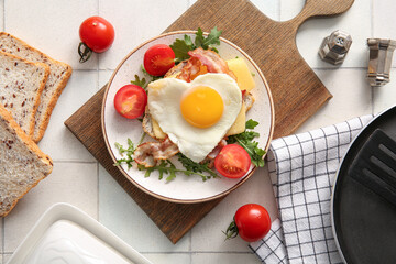 Composition with tasty fried egg, toasts, bacon, tomatoes and arugula in plate on light tile background