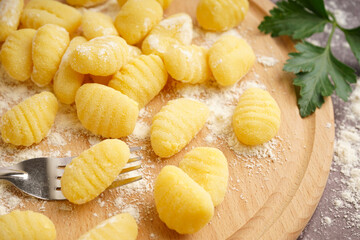 Wooden board with tasty gnocchi, flour and parsley on grunge background, closeup