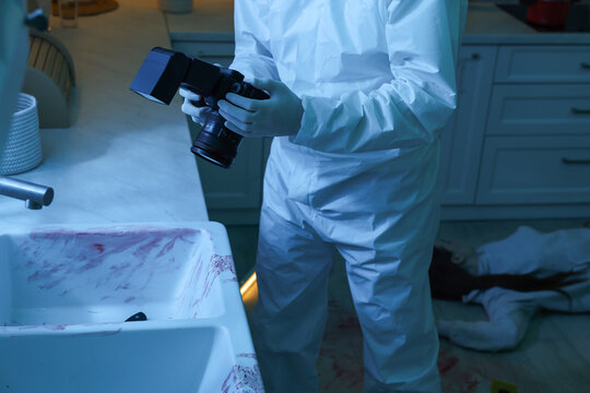 Forensic expert with camera working at crime scene in dark room, closeup