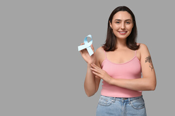 Pretty young woman with light blue ribbon on grey background. Prostate cancer awareness concept