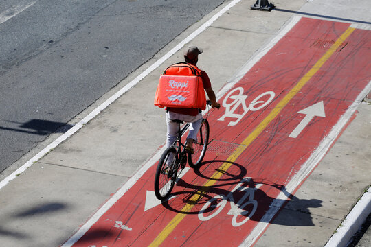 Sao Paulo, SP, Brazil - May 1, 2021: Delivery boy working for Rappi app ride his bike through the cycling lane path.