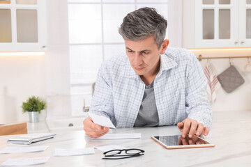 Obraz premium Man paying bills with tablet at white marble table indoors