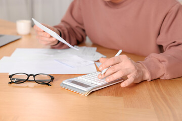 Paying bills. Man with different invoices using calculator at wooden table indoors, closeup