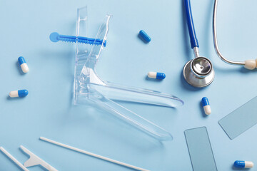 Stethoscope with gynecological speculum, pap smear test tools and pills on blue background