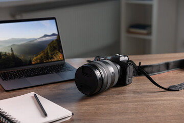 Professional photo camera, laptop and notepad on wooden desk indoors