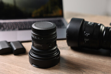 Professional photo camera, lens and laptop on wooden desk, selective focus