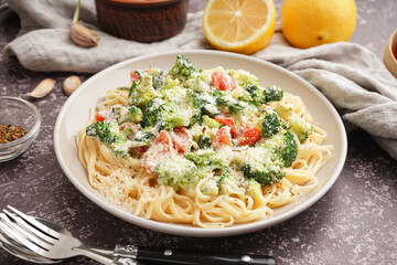 Plate of tasty pasta with broccoli, tomatoes and cutlery on grunge grey background