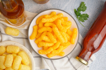 Plates with different tasty salty corn sticks and sauce on light background