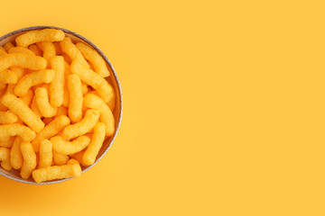 Bowl with tasty salty corn sticks on orange background