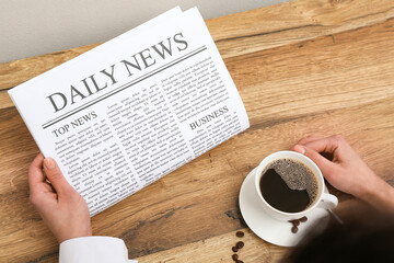 Female hands with newspaper and cup of coffee on wooden table