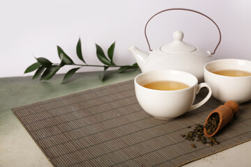 Bamboo mat with teapot, cup of tea and leaves on grunge table against white background