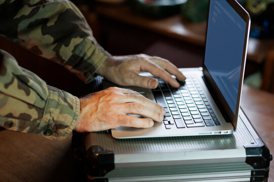 Military personnel , hacker, types on laptop in a casual indoor setting