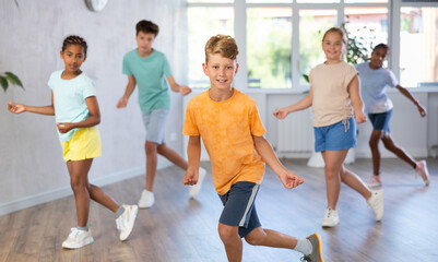 Fototapeta premium Positive juvenile boy engaged in Rock 'n' Roll dance together with children's group in training room during workout session