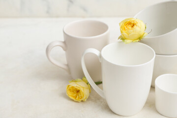 Composition with clean cups and yellow roses on table near marble wall