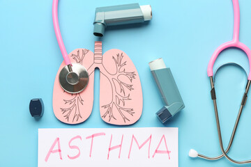 Inhalers, paper lungs, stethoscope and paper sheet with text ASTHMA on blue background, closeup