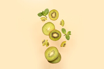 Cut ripe kiwi and mint leaves flying on color background