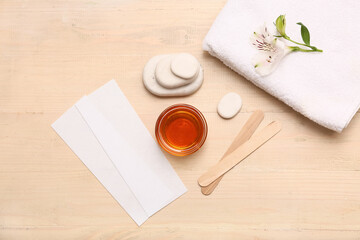 GLass bowl with sugaring paste, wax strips, sticks, spa stones and alstroemeria flower on light wooden background