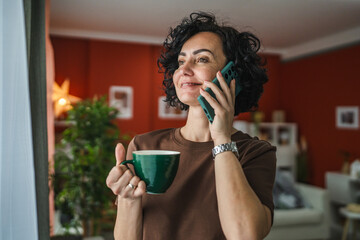 mature curly hair woman talk on mobile phone while drink coffee indoor