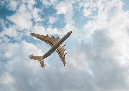 The underside of An-225 flying against cloudy sky. Looking up at the huge six-engined Mriya cargo plane on a sunny day. Hostomel, Ukraine - August 22 2021.