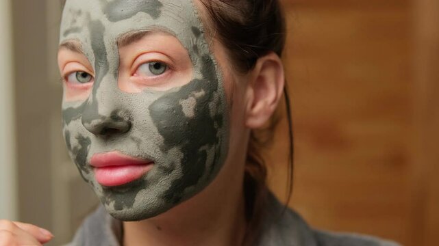 Close-Up of a woman with an almost dry gray clay face mask gently touches her skin, feeling its texture while waiting for it to fully set. Beauty treatments for skin care