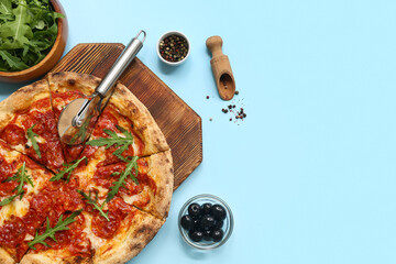 Composition with tasty pizza, ingredients and cutter on blue background
