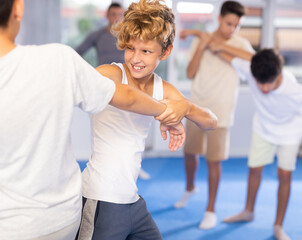 Willing junior attendee of self-defense classes fighting with his opponent in sports hall