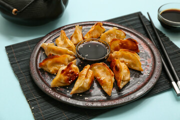 Plate with fried Japanese gyoza and bowls of soy sauce on blue background, closeup