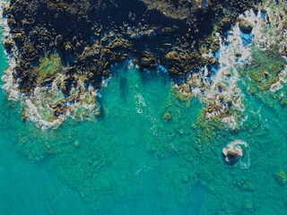 Tropical Bright Blue Water meets Black Sand and Rocks in Drone Shot from Above