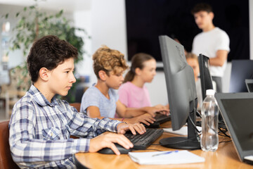 Minor male student sitting at computer together with other attendees of IT courses