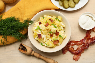 Bowl of tasty potato salad with green onion, bacon, dill and sour cream on beige wooden background