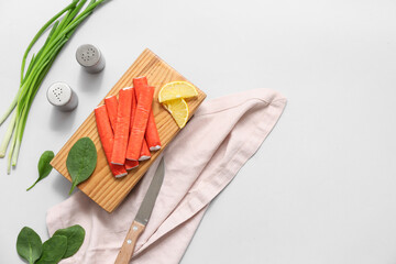 Wooden board with tasty crab sticks, slices of lemon, spinach leaves and green onion on grey background © Pixel-Shot