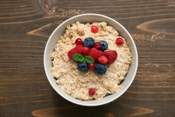 Bowl with tasty oatmeal and berries on wooden background