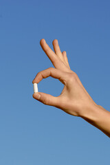 Vertical image of a female hand holding a white pill with her fingers on a blue background. Pharmacy concept, health care. Image for your design
