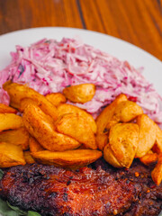 Simple meal with pork belly, potato wedges and pink coleslaw on white plate. Fine dinner with simple products.