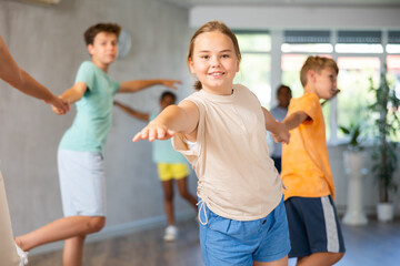 Fototapeta premium Smiling cute tween girl practicing vigorous dance in pair with boy during group training in kids dance studio..
