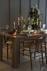 Christmas table setting with stylish dishware, glasses and burning candles in festive decorated room