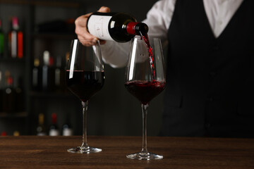 Professional sommelier pouring red wine into glasses at wooden table indoors, closeup