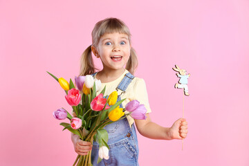 Happy little girl with bouquet of tulips and decorative Easter bunny on pink background