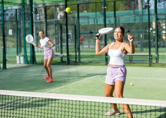 Obraz premium Two active women tennis players, playing padel on an outdoor court, using rackets to hit the ball